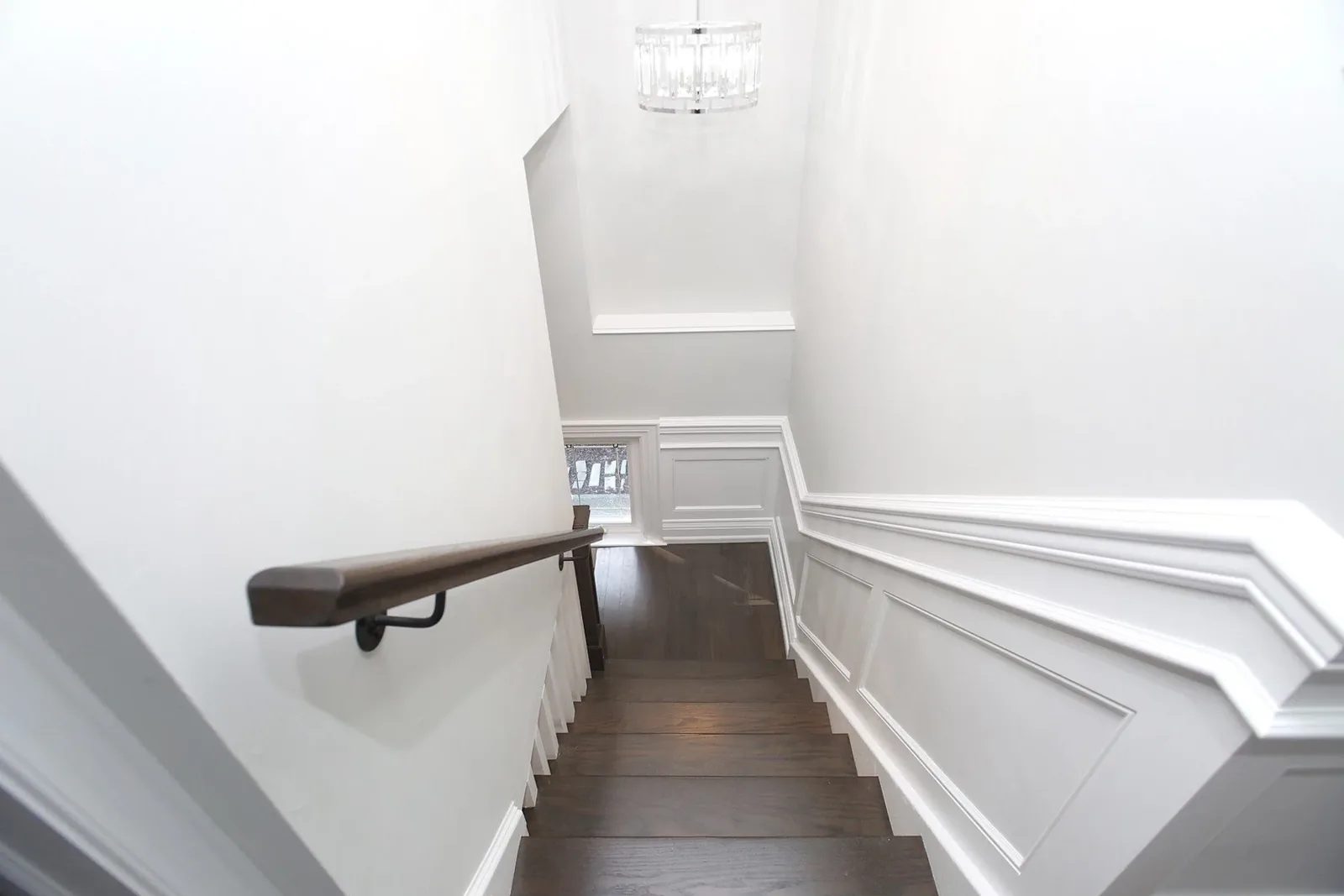 Bright white stair hall with dark wood treads, classic wall panelling, and a modern ceiling light.