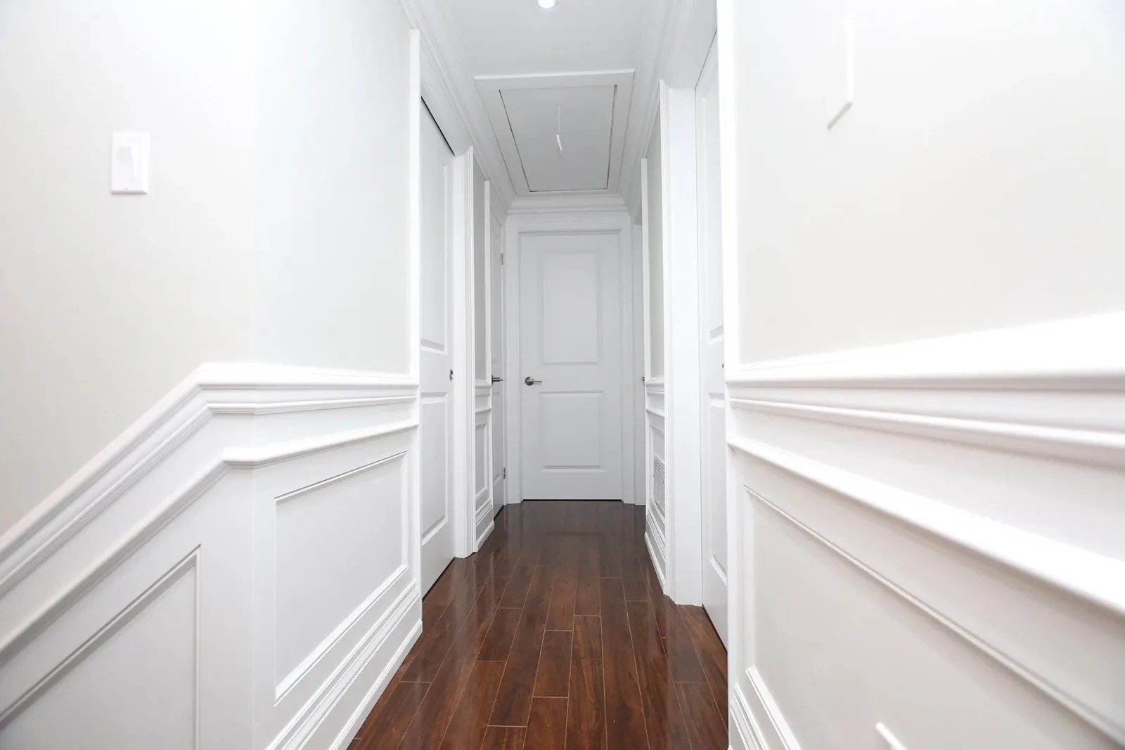 Finished hallway with a warm white colour palette, classic wall moulding, and dark wood floors.