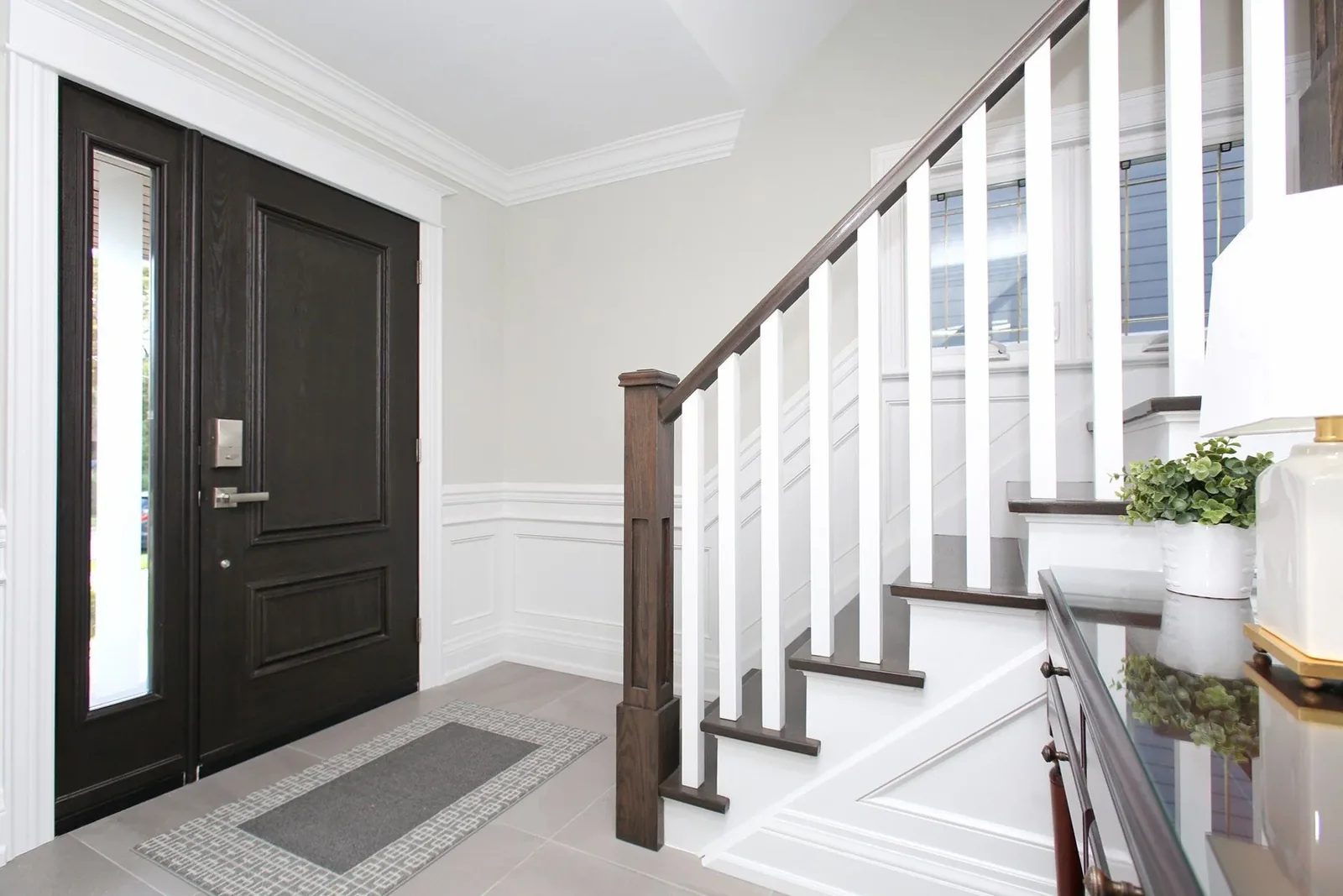 Bright transitional entry with dark wood front door, white millwork, and staircase with contrasting treads.