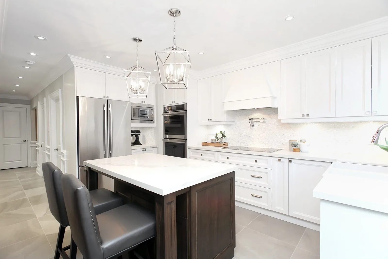 Bright white kitchen with a quartz island, stainless appliances, and grey tile flooring.
