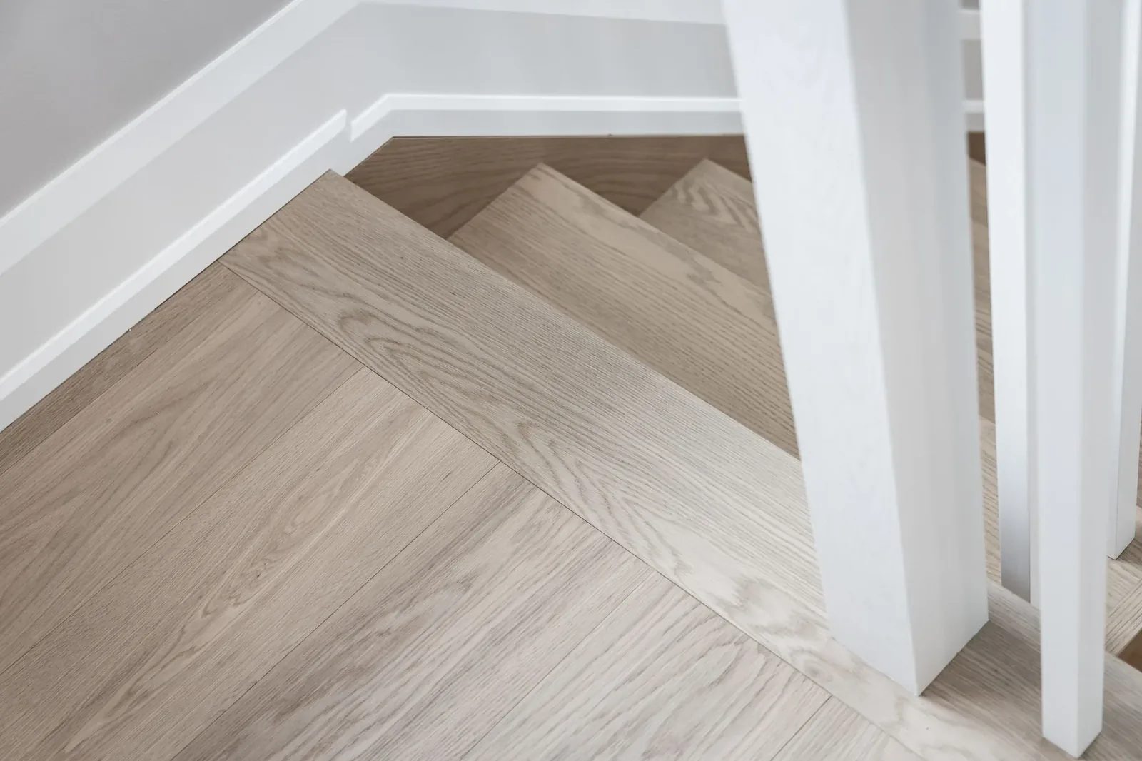 Pale oak stair treads wrapping a white newel base where the staircase meets the oak floor.