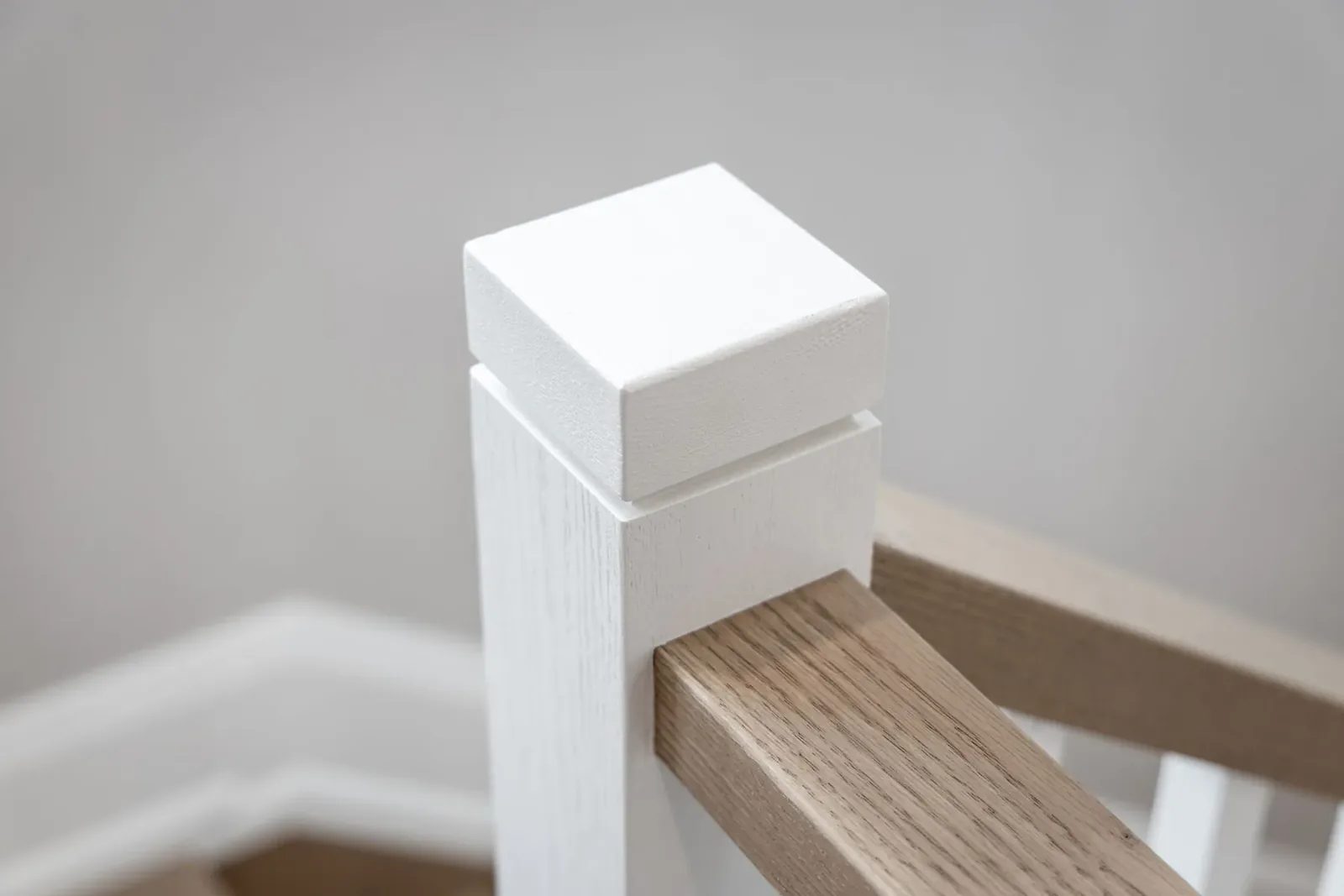 A square white newel post meets a pale wood handrail at the staircase landing.