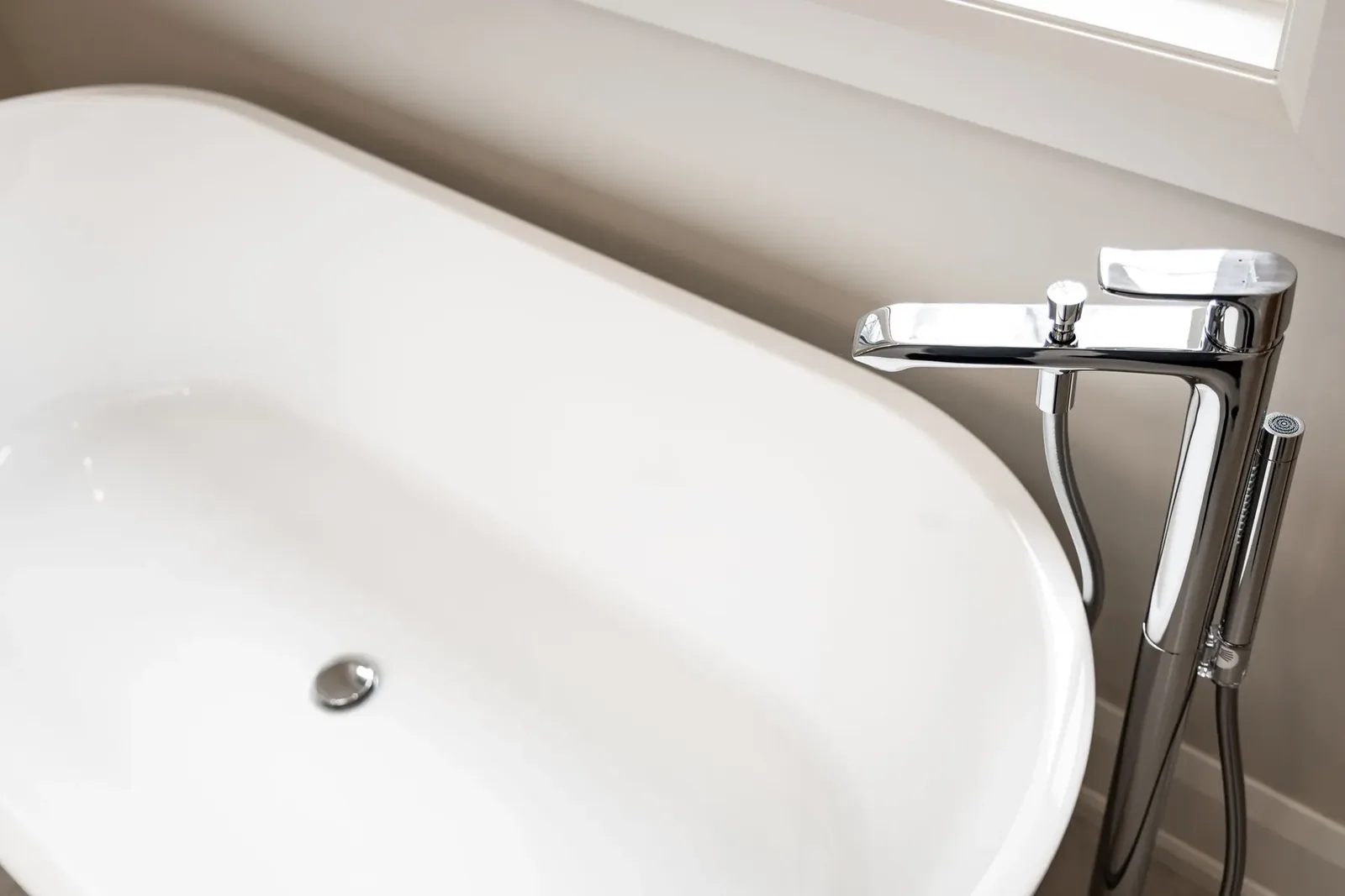 A polished chrome floor-mounted tub filler and hand shower stand beside a white freestanding bathtub in the main bath.