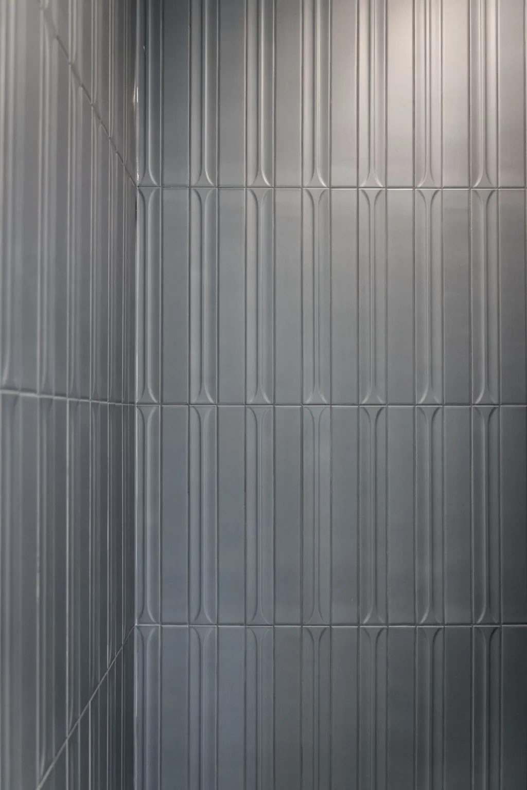 Glossy blue-grey fluted tiles cover the inside corner of the main bath shower.