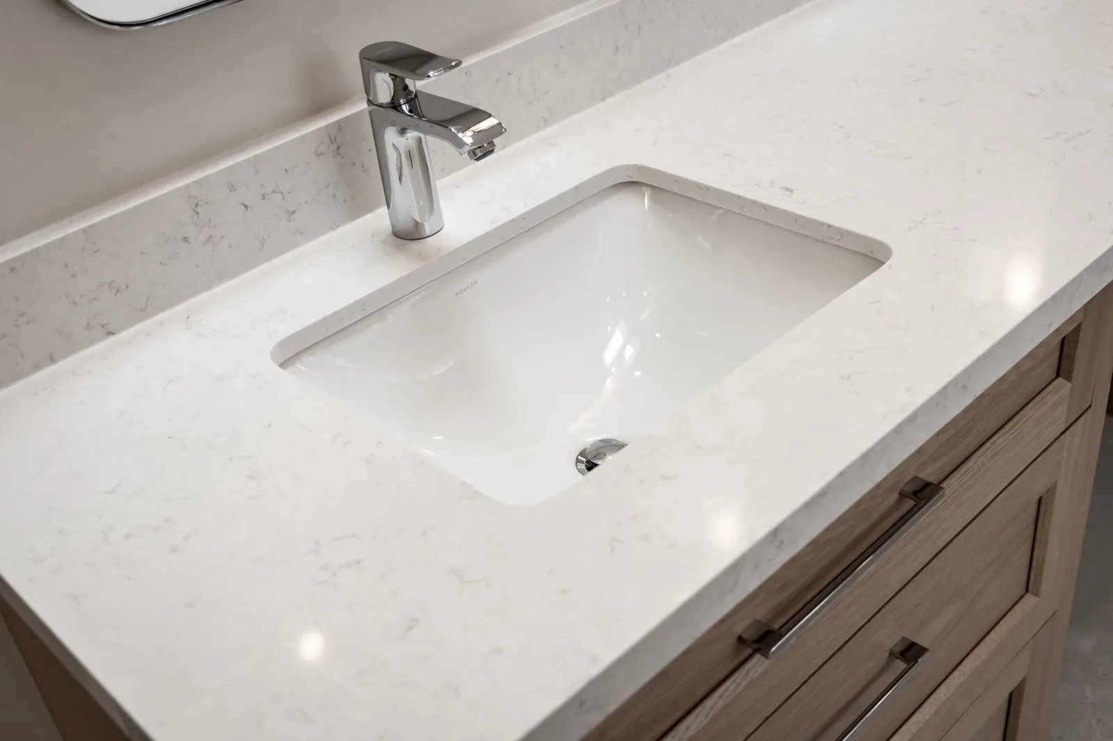 White quartz vanity top with an undermount sink and chrome single-handle faucet over light oak drawers.