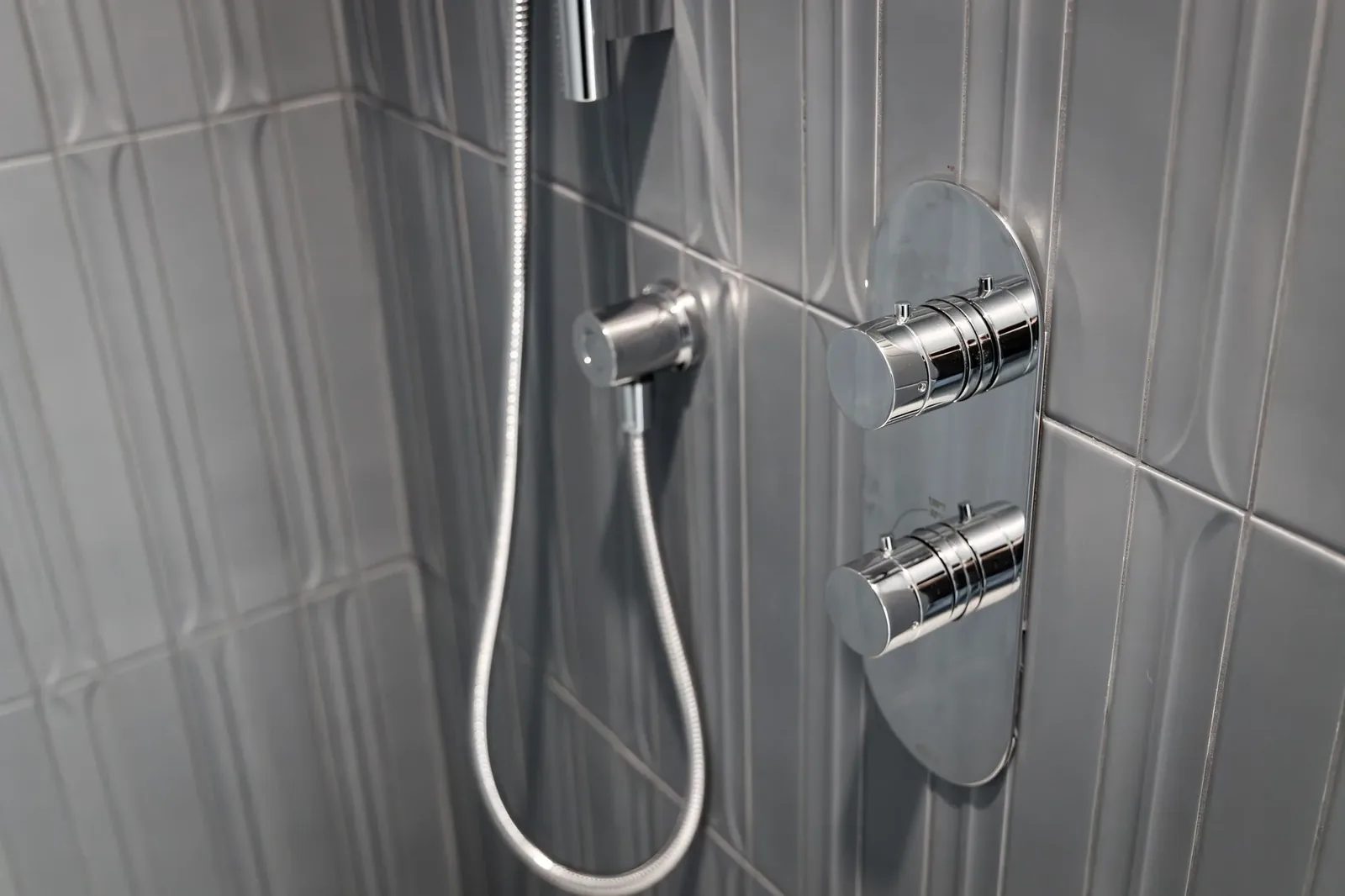 Chrome thermostatic shower controls and handheld sprayer set against grey fluted tile.