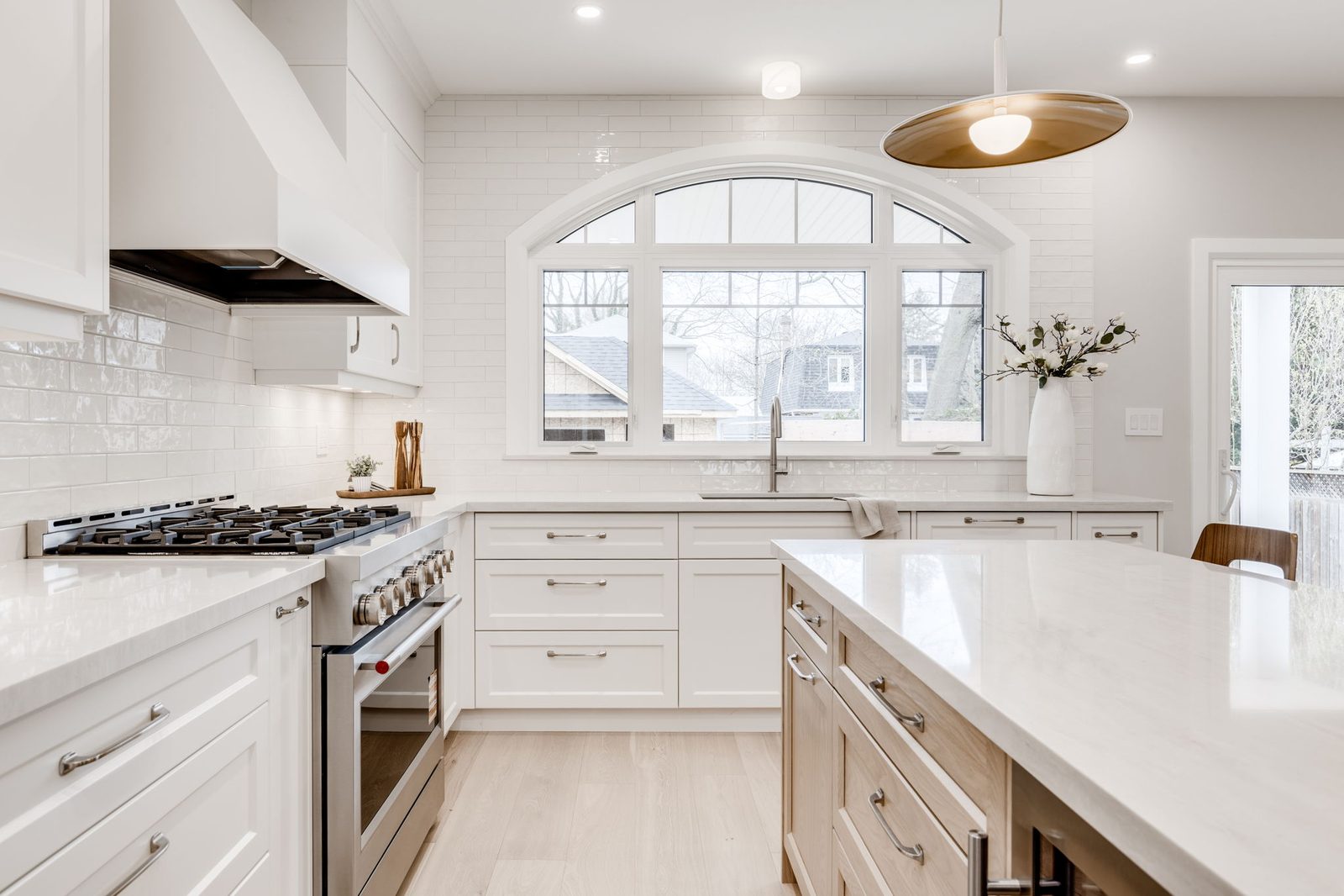 Range wall with a custom white hood surround, a glazed subway backsplash and the arched window over the sink beside it.