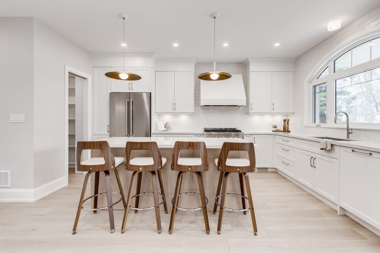 White shaker kitchen with a quartz-topped oak island, walnut and white stools and warm brass pendants over pale oak flooring.