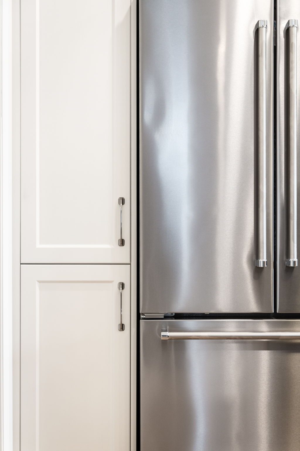 Integrated panelled tall cabinet beside the stainless french-door fridge, showing the flush cabinetry surround.