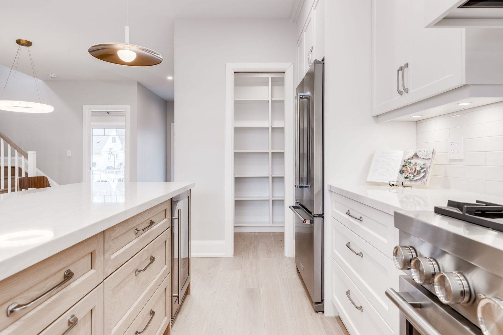 Walk-in pantry standing open beside the range, with full-height white shelving inside.