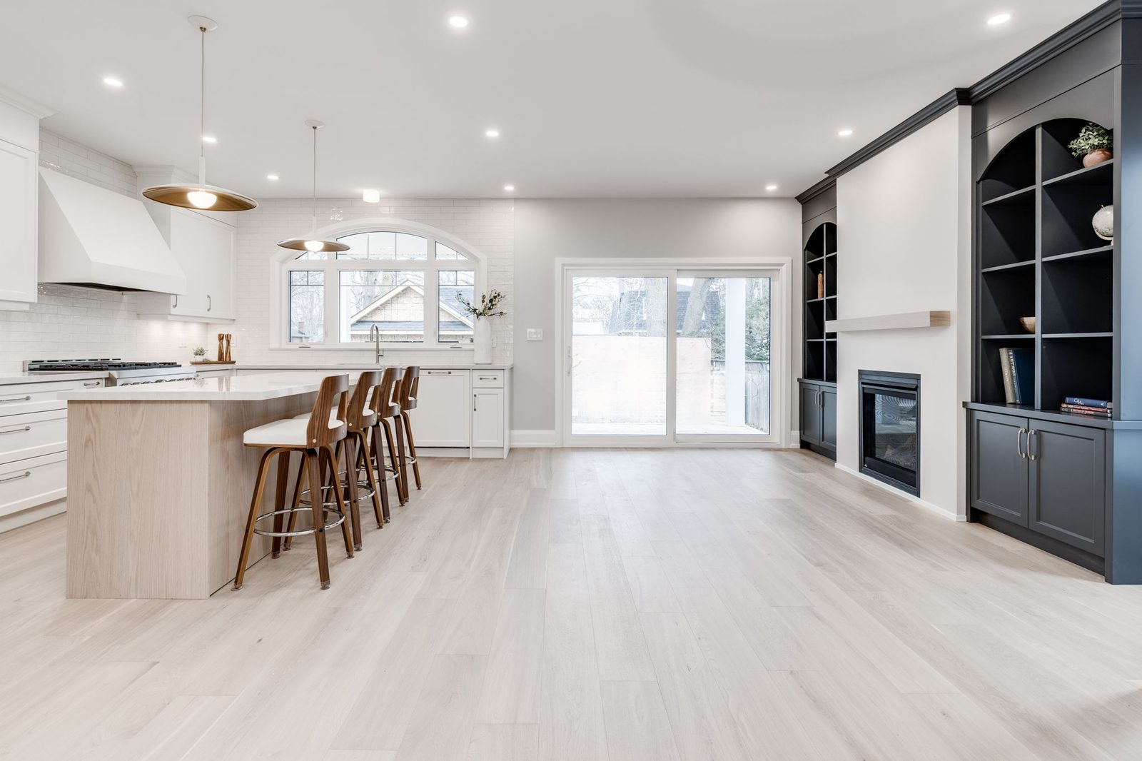 Open-plan main floor with the kitchen island on one side and the dark built-ins and fireplace on the other, joined by pale oak floors.
