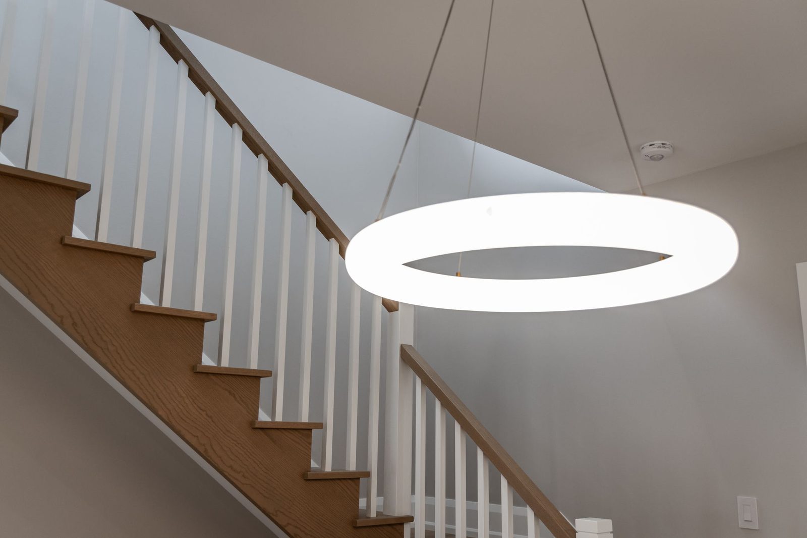 Oak staircase with white square balusters and an oak handrail beneath a glowing ring pendant.