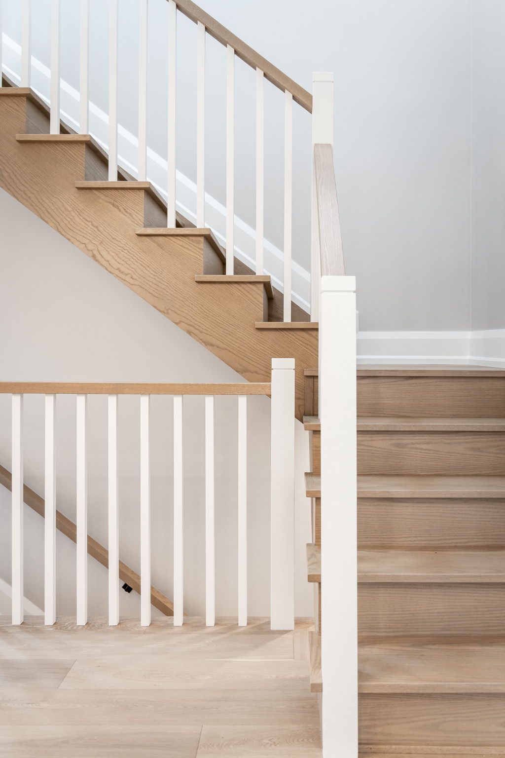 Full flight of the staircase, with oak treads, white risers, square balusters and the newel post.