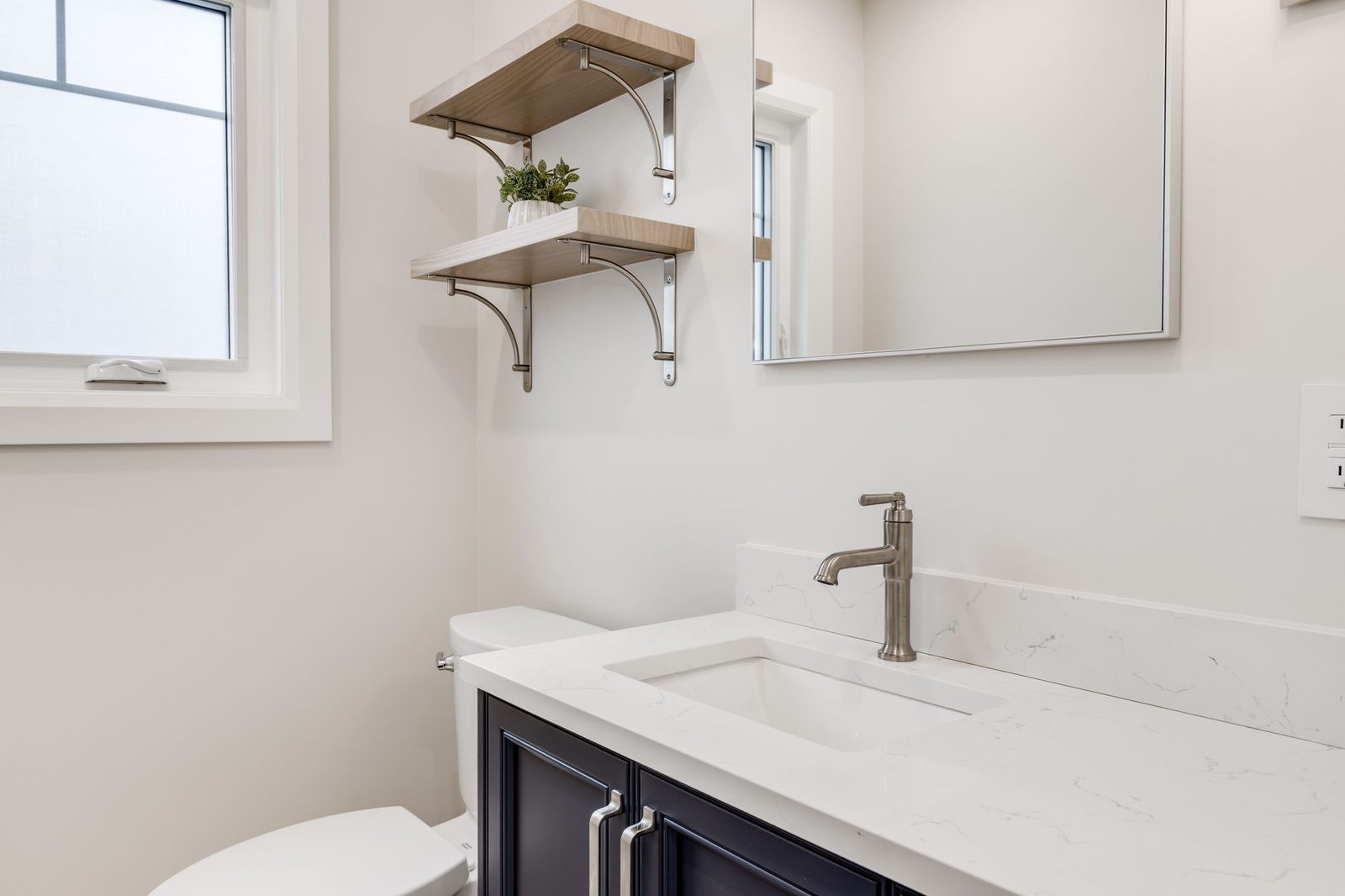 Powder room with a dark vanity under a quartz counter, a brushed nickel faucet and oak wall shelves on curved brackets.