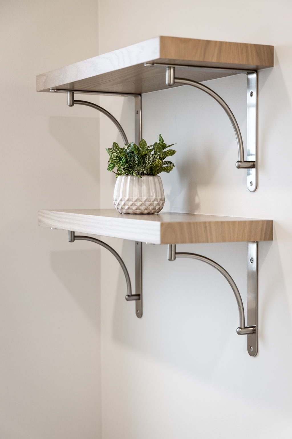 Two oak floating shelves carried on curved brushed nickel brackets.