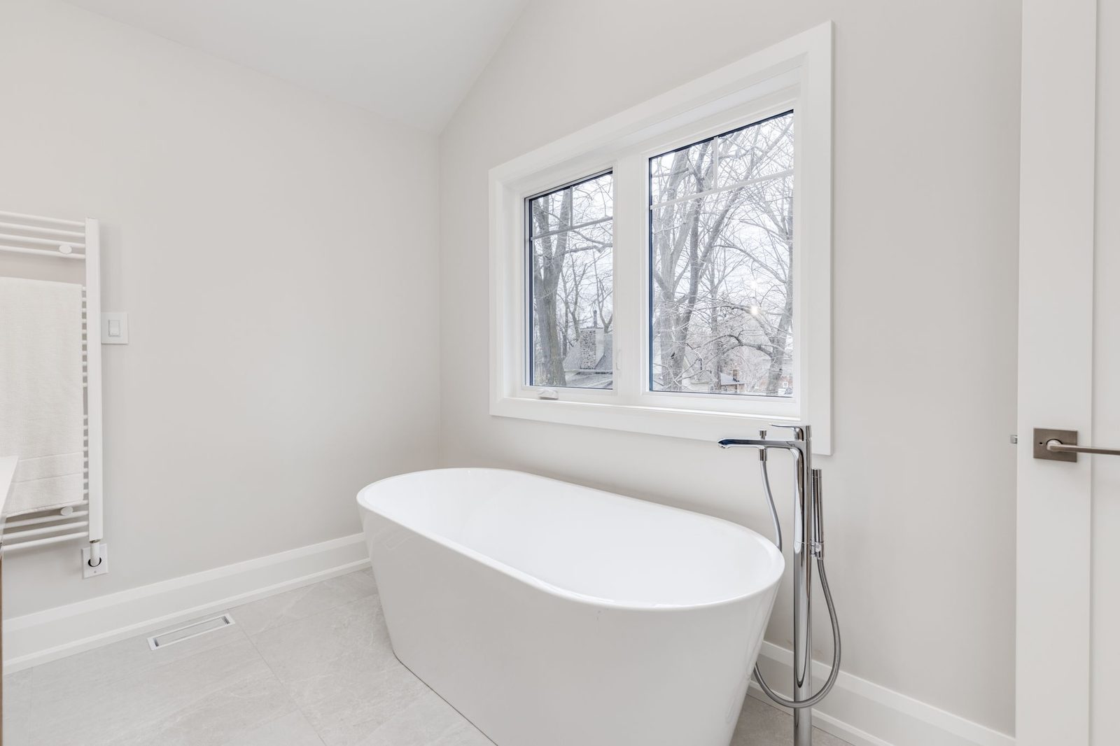 Freestanding tub beneath the window in the vaulted ensuite, with a floor-mounted chrome filler.