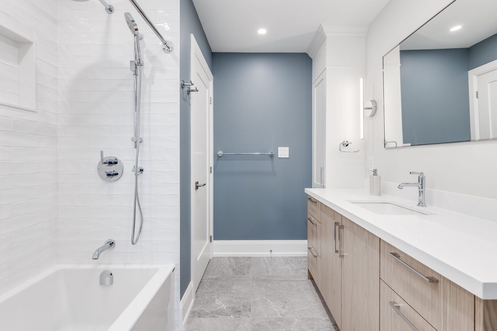 Tub and shower wall in white tile with the vanity opposite and the blue accent wall between them.