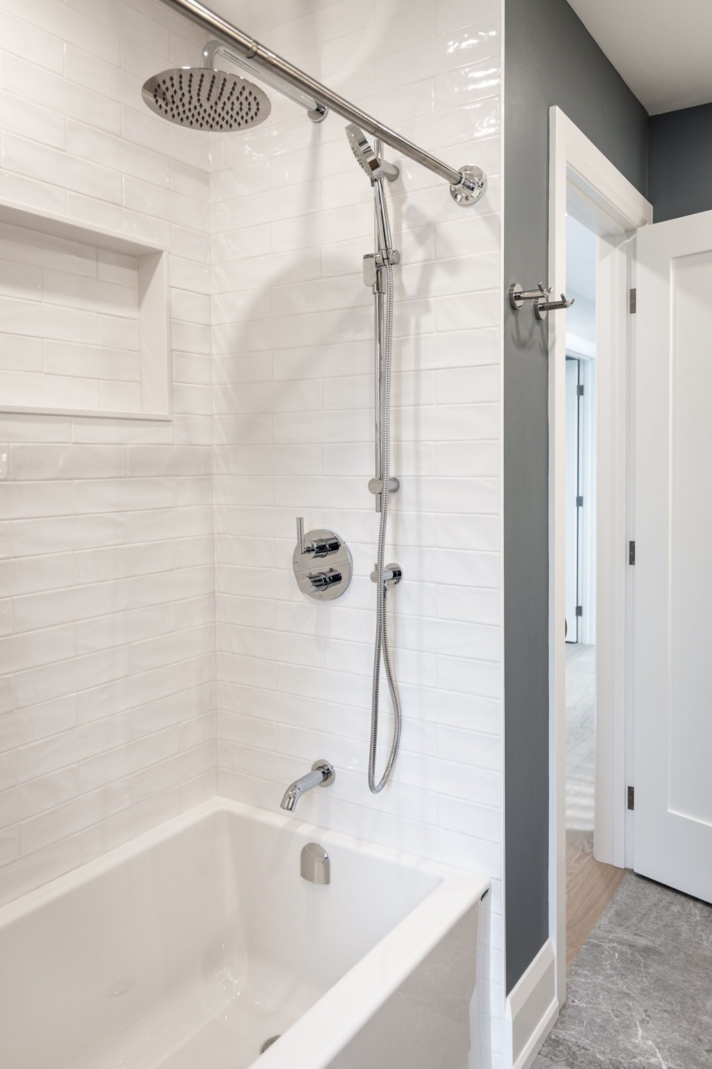 Stacked white tile shower over the tub with a recessed niche and a chrome rainfall head.