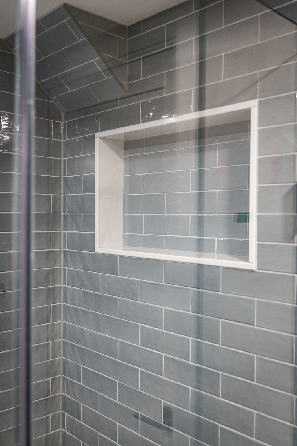 Grey subway shower with a white-trimmed recessed niche behind the glass panel.