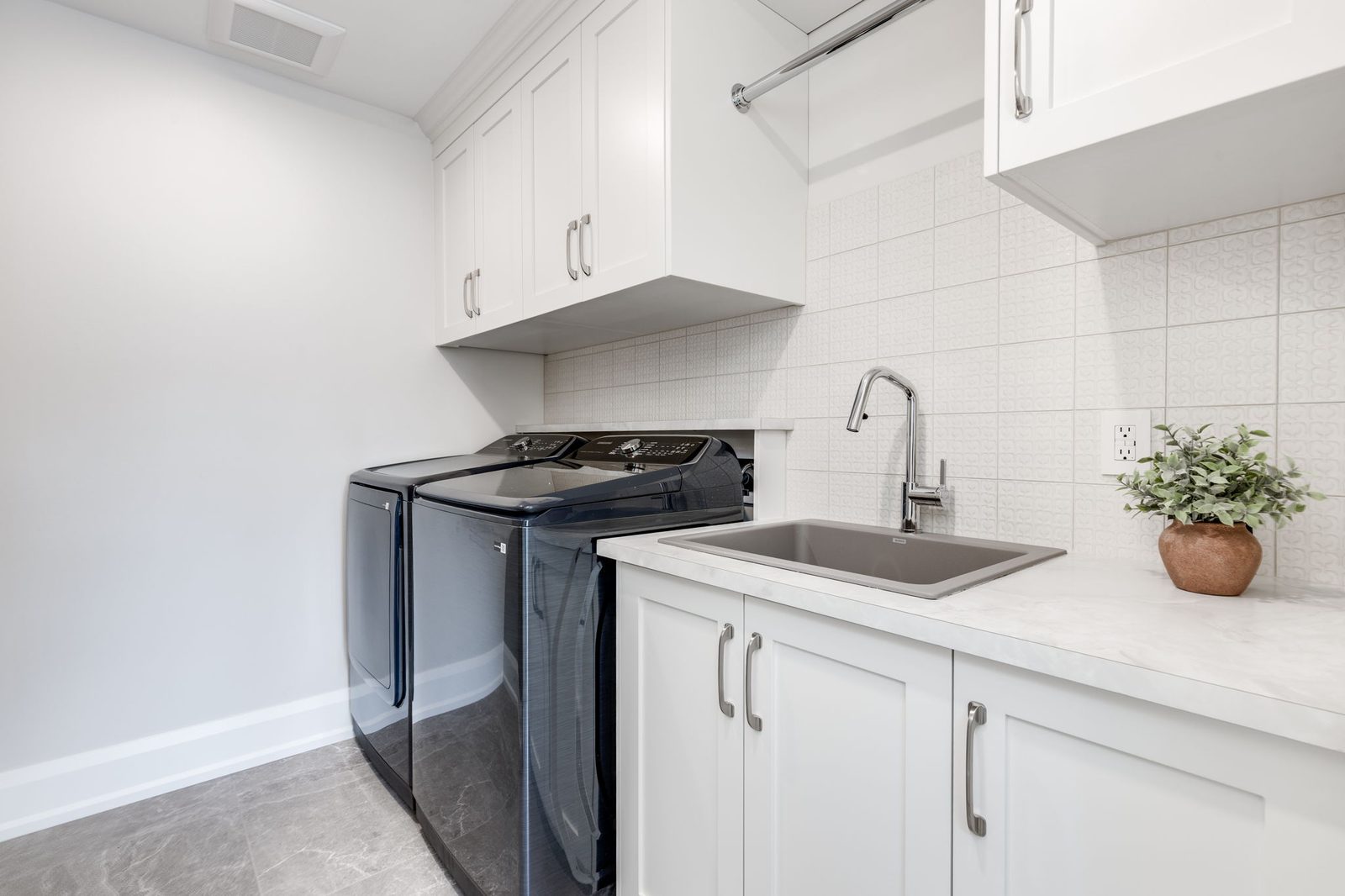 Laundry with white shaker upper cabinetry, a counter run over the machines and a textured white tile backsplash.