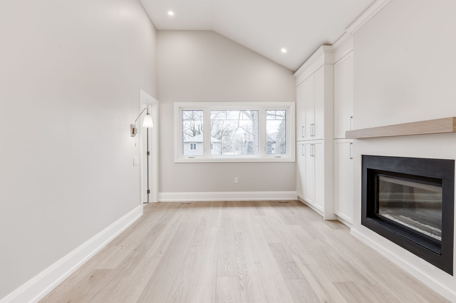 Vaulted primary bedroom with the linear fireplace, the oak mantel shelf and a wall of white built-in wardrobes.