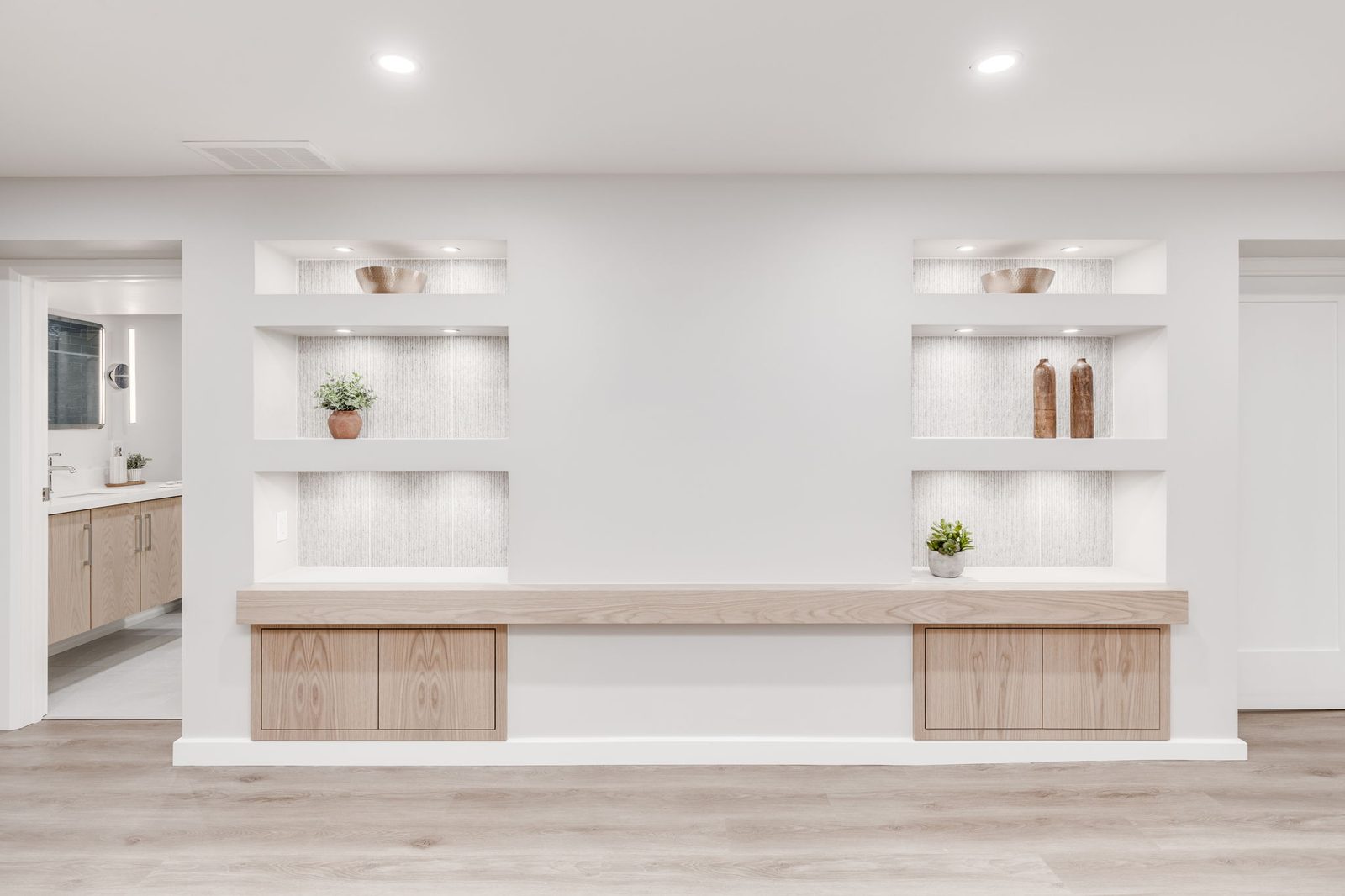 Basement feature wall with lit display niches above a long floating oak bench and matching cabinet doors.