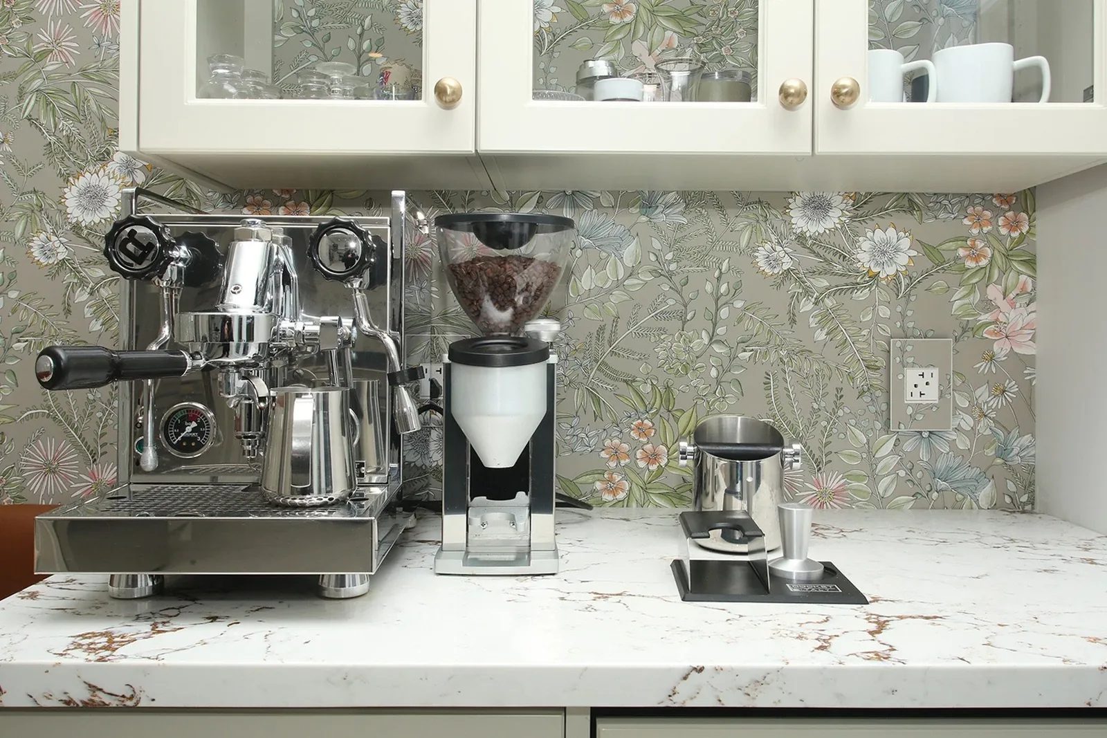 Bright kitchen coffee station with floral wallcovering, warm white cabinetry, quartz counter, and brass hardware.