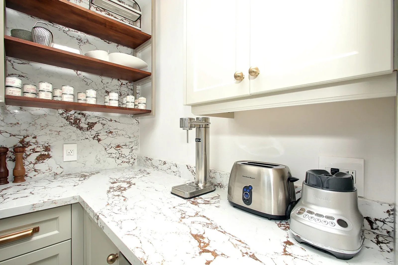 Warm white kitchen corner with dramatic quartz veining, walnut shelves, and brass hardware in a finished renovation.
