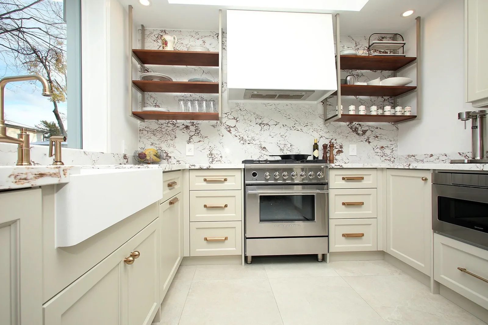 Bright white kitchen with veined stone walls, walnut shelves, brass hardware and a centred range.