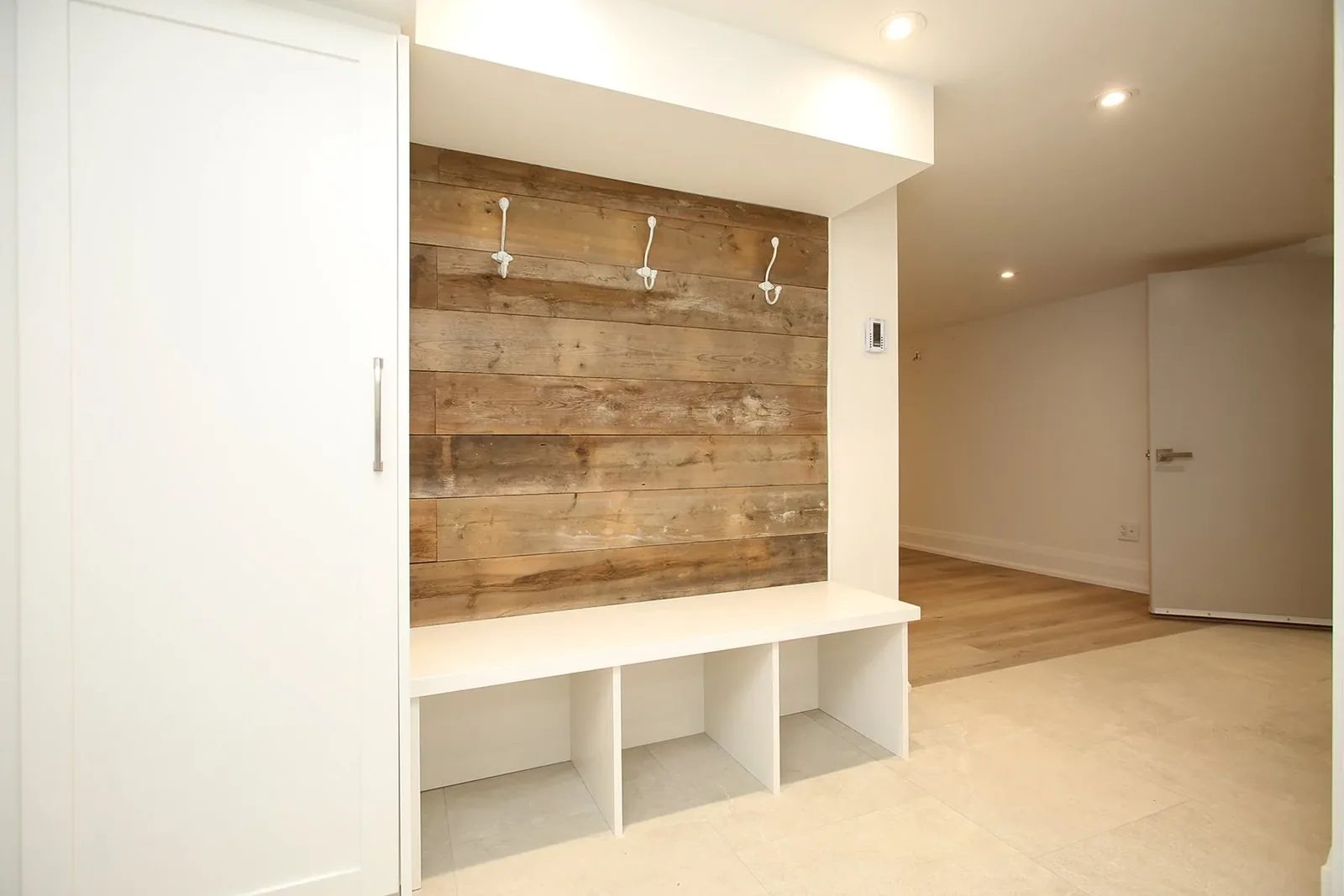 Wider finished basement showing the reclaimed plank mudroom nook, built in bench, recessed lights, and adjoining living area.