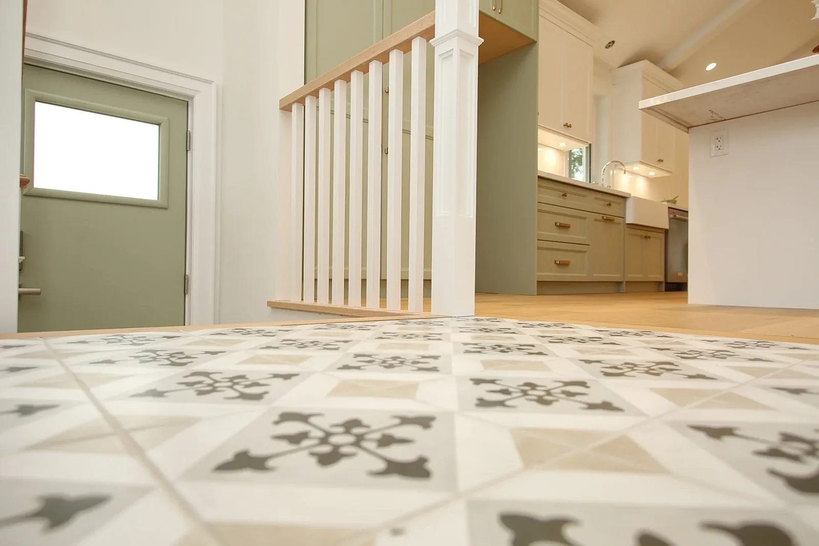 Low angle of the patterned foyer tile with the sage side door and sage kitchen cabinetry softly in focus beyond.