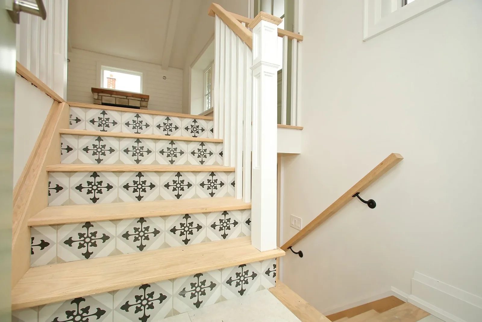 Oak stair treads with black and white patterned tile risers rising past white spindles to a bright upper landing.