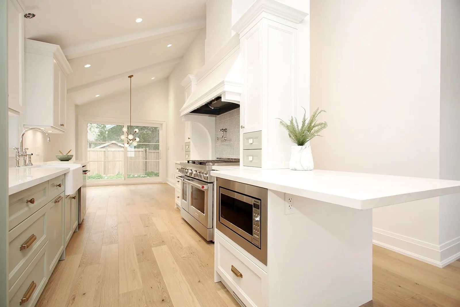 Vaulted galley kitchen in white and sage with a pro range, peninsula, and dining area beyond sliding glass doors.