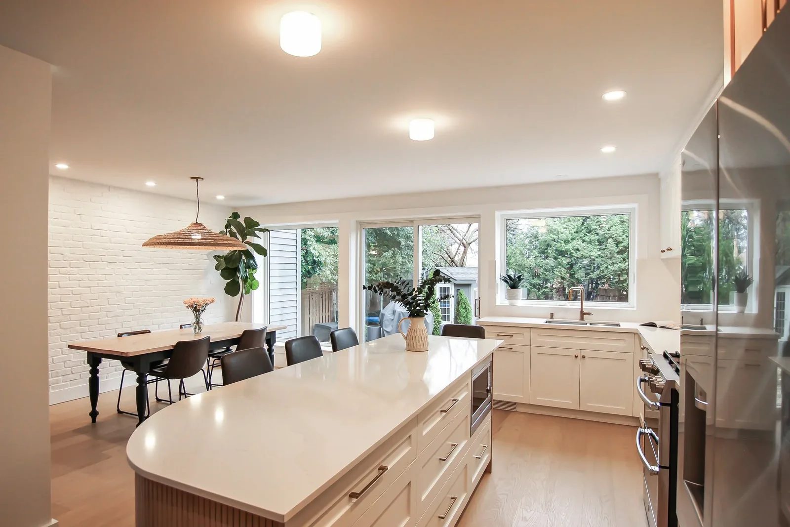 Bright renovated kitchen with a large centre island, oak floors, and wide windows facing the yard.