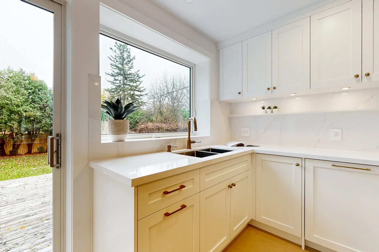 Bright white kitchen corner with quartz counters, brass hardware, and a large window by the sink.
