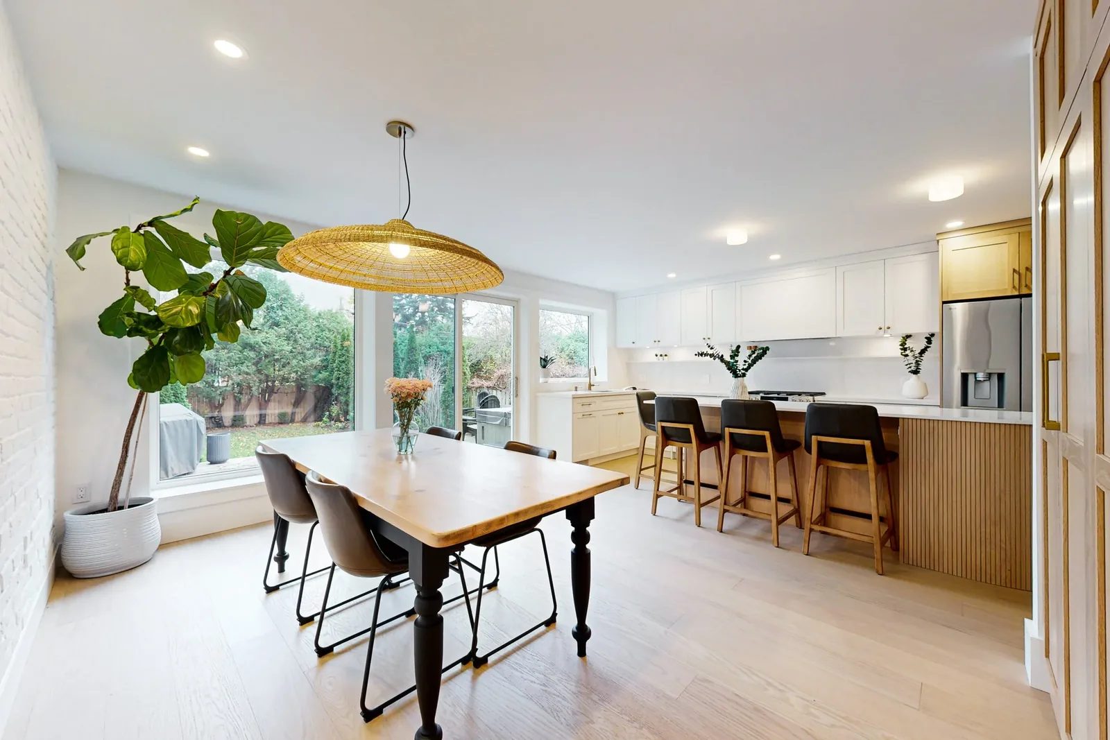 Bright open kitchen and dining area with white cabinetry, oak accents, large windows, and island seating.