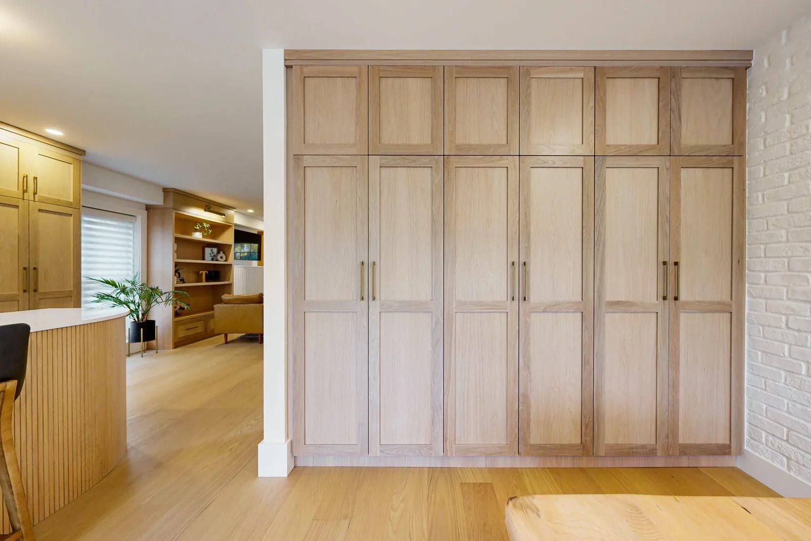 Natural oak cabinetry anchors an open concept room with light floors, white walls and organised storage.