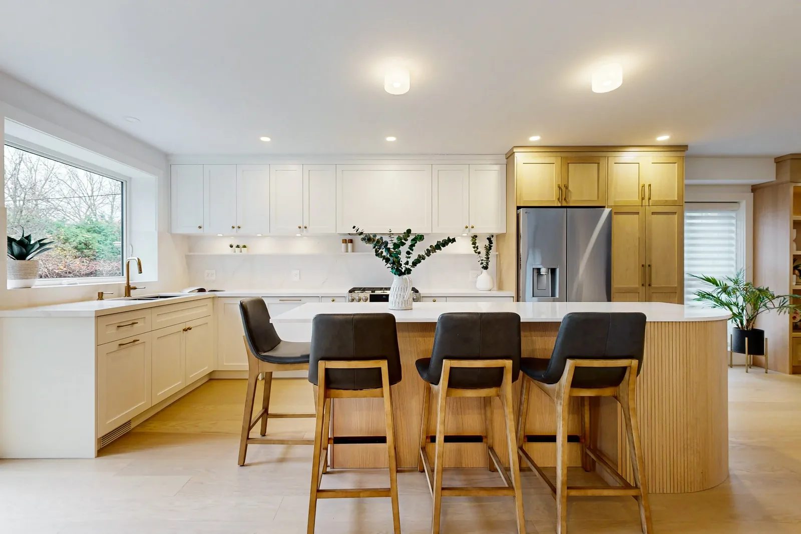 Bright open kitchen with white cabinetry, oak island seating and brass accents in a finished renovation.