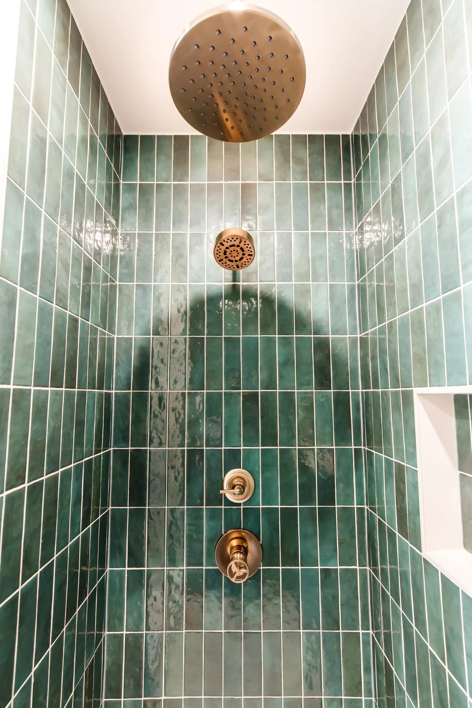 Upward view of emerald tile shower showing brass rainfall head and valve stack.