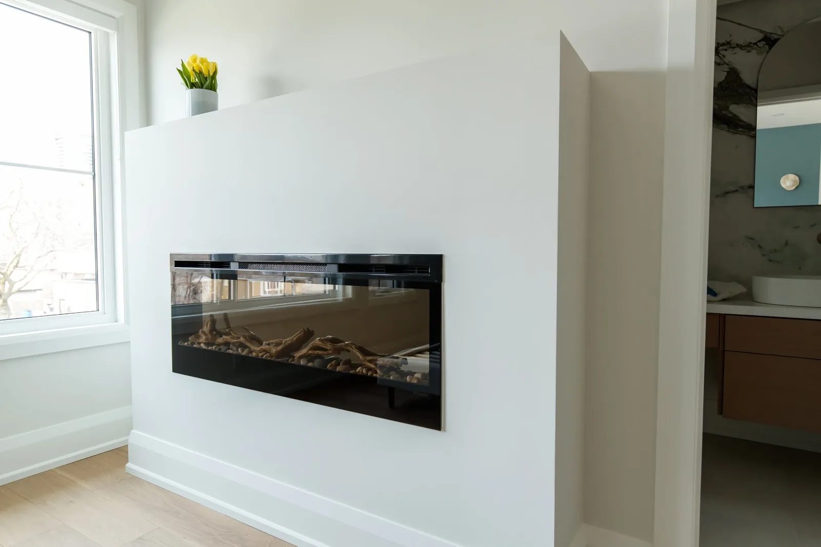 Linear electric fireplace on a white partition wall with a yellow tulip accent above.