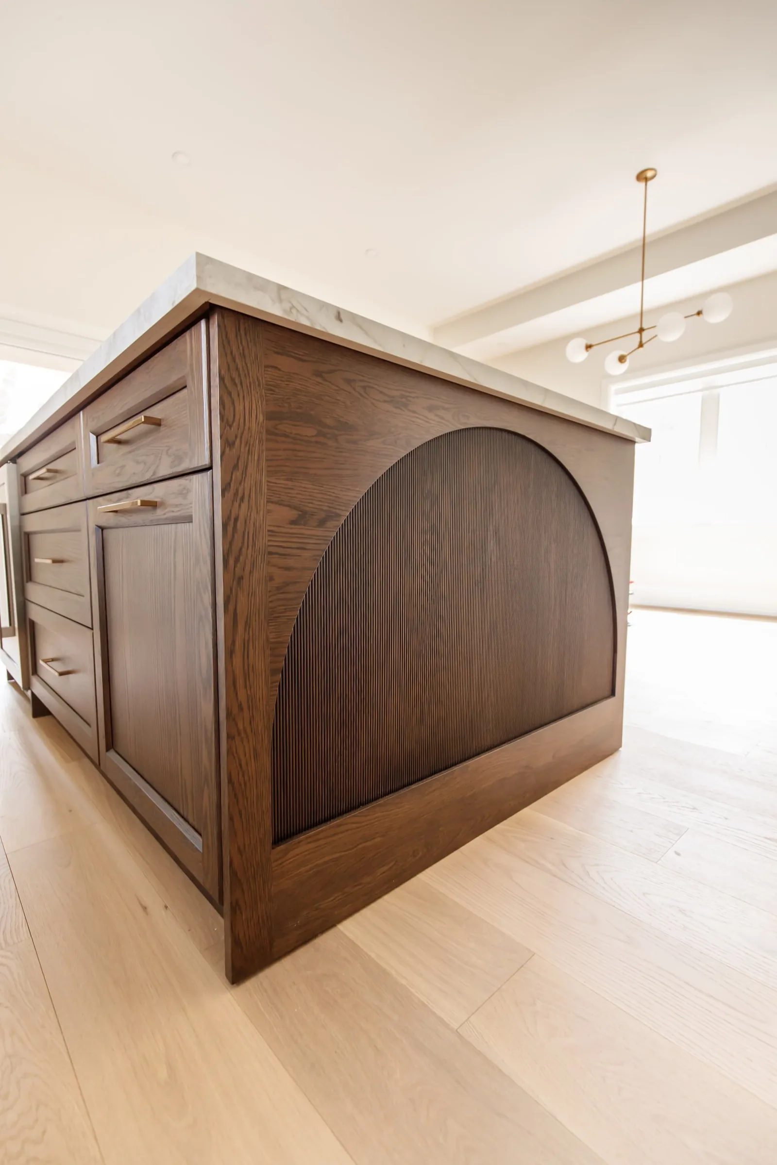 Close detail of a walnut island end panel with reeded arch and marble waterfall edge.