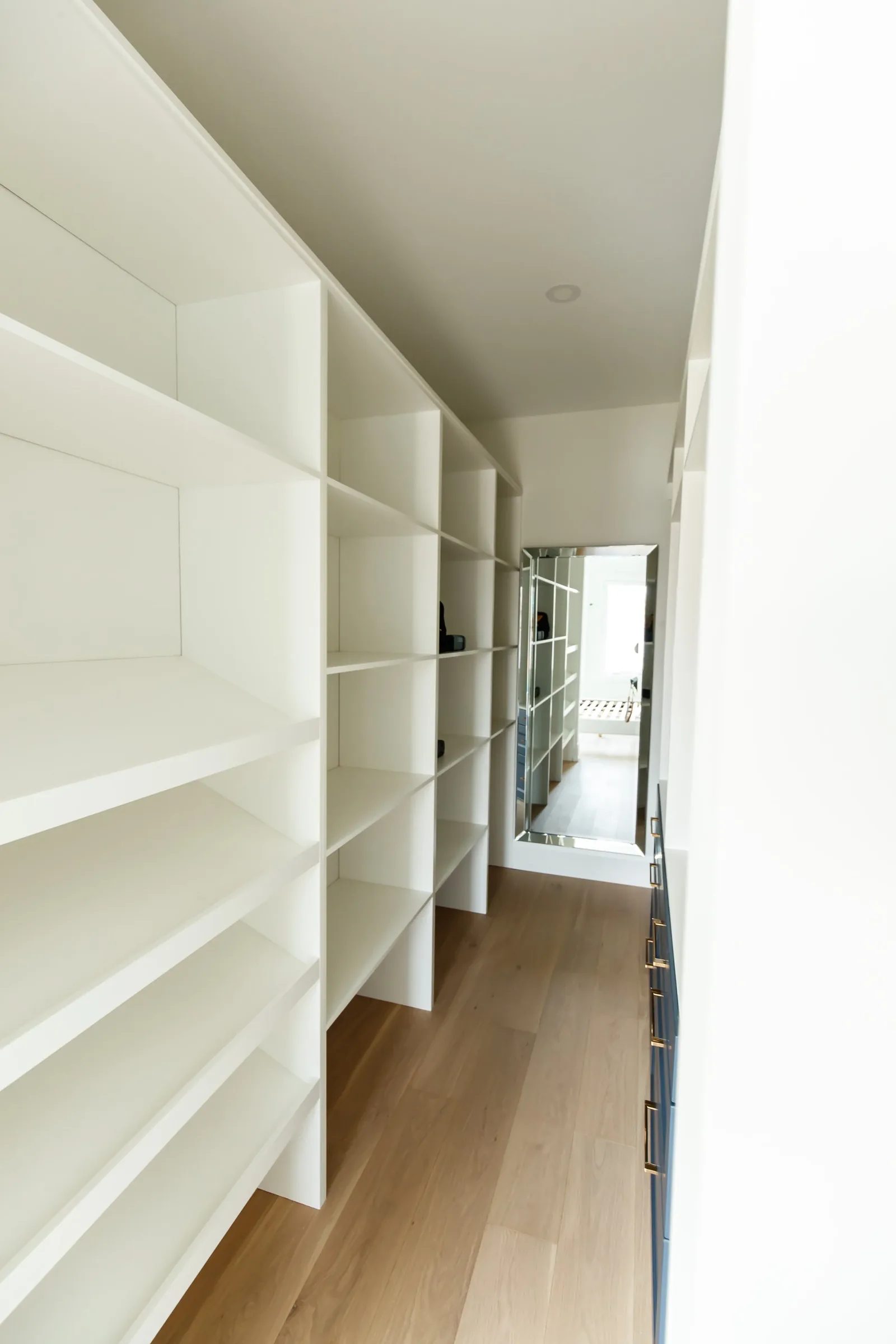 Warm white built-in shelving lines an organised closet corridor with natural oak flooring.
