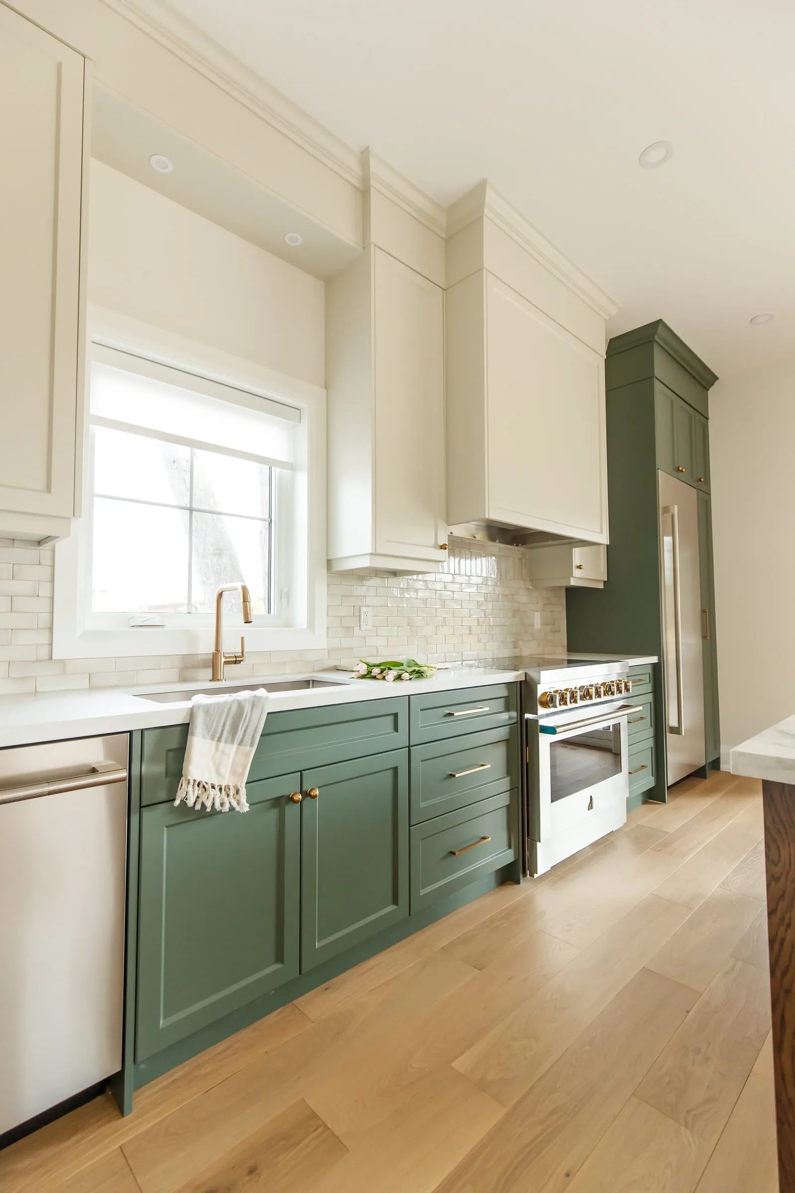 Vertical shot of the green lower cabinets and cream uppers running to a pro range and panel-ready fridge column.