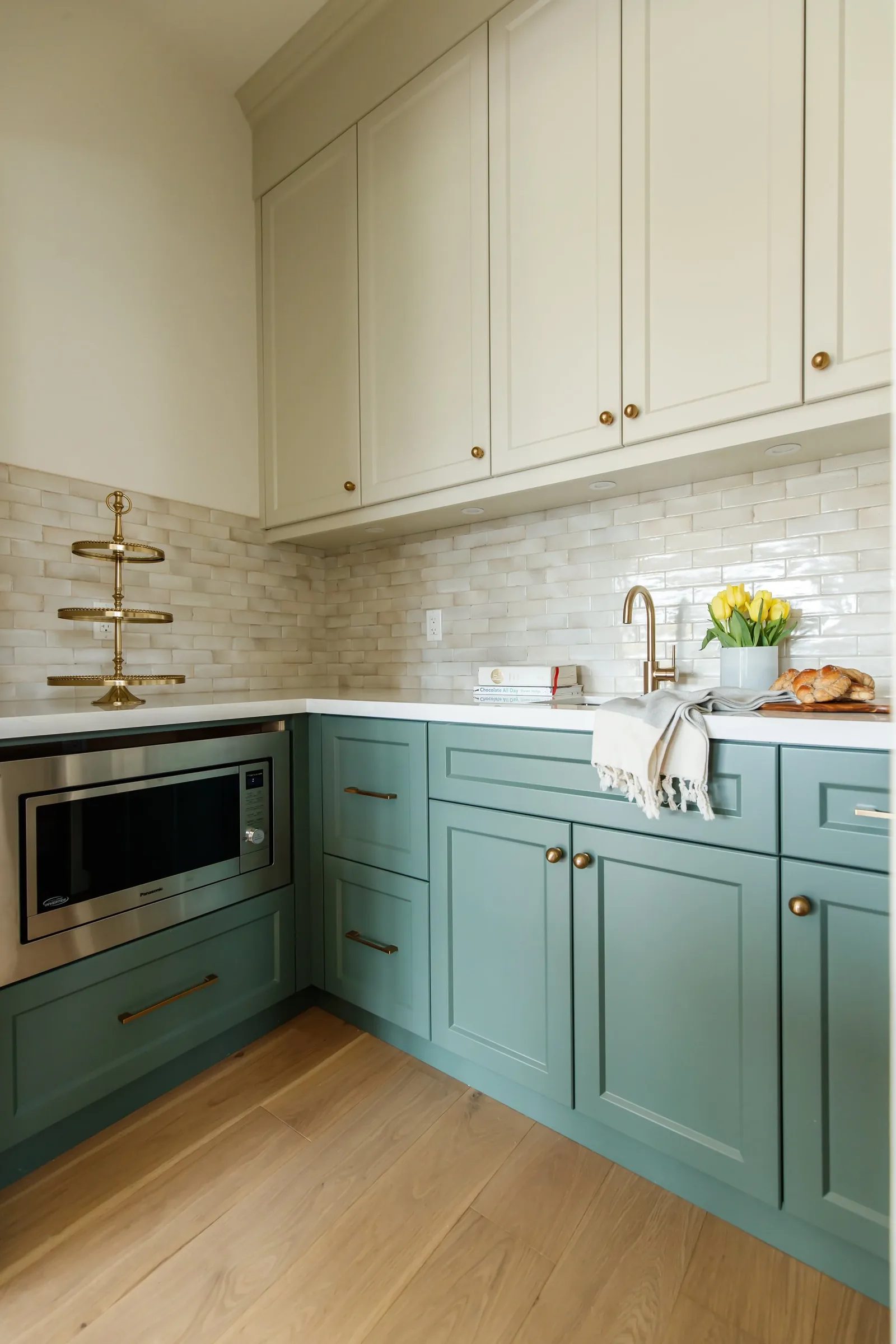 Teal lower cabinetry with cream uppers, brass pulls and a handmade zellige backsplash.