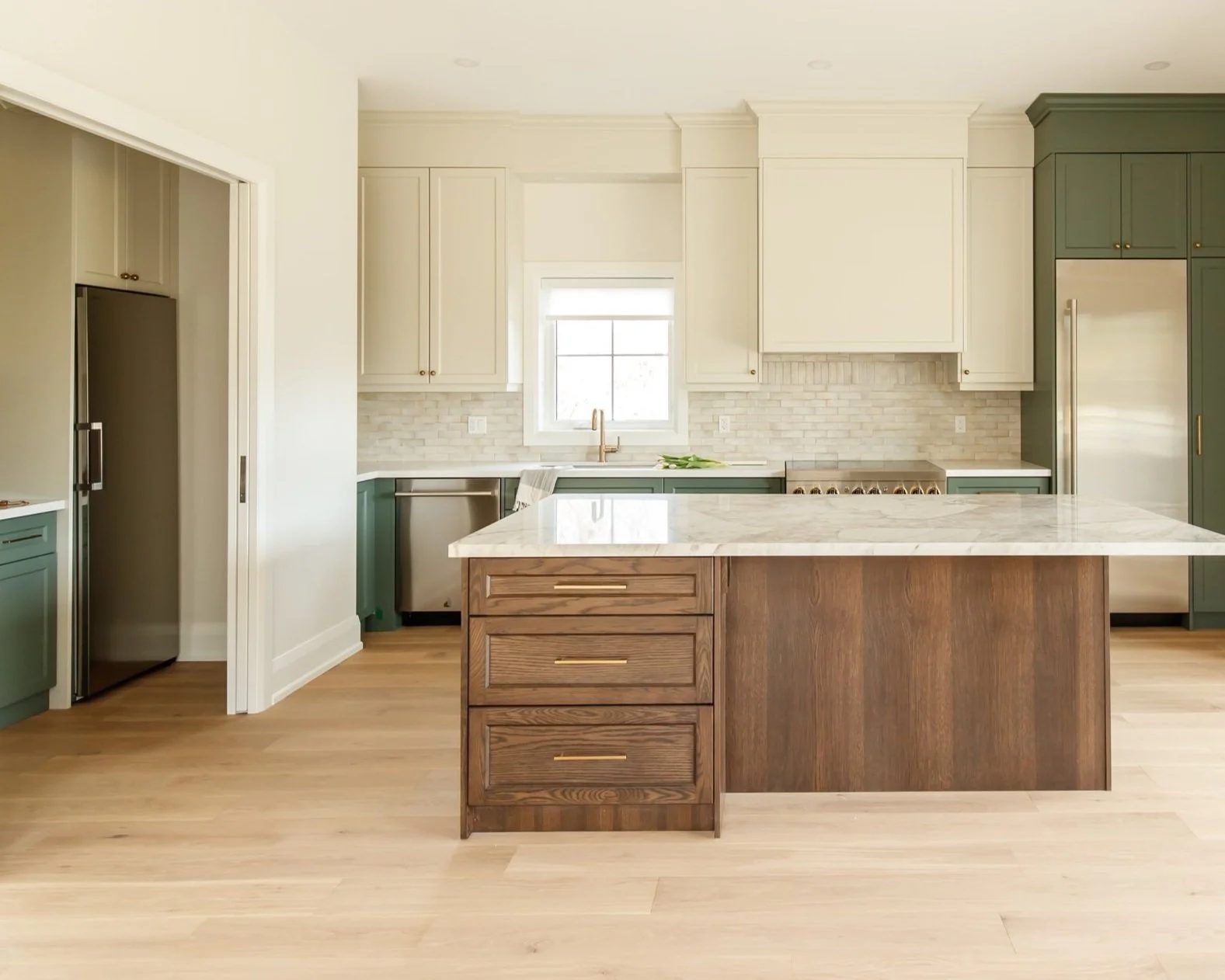 Open plan kitchen view with a wide stained oak island facing a glass slider and a tall green pantry column.