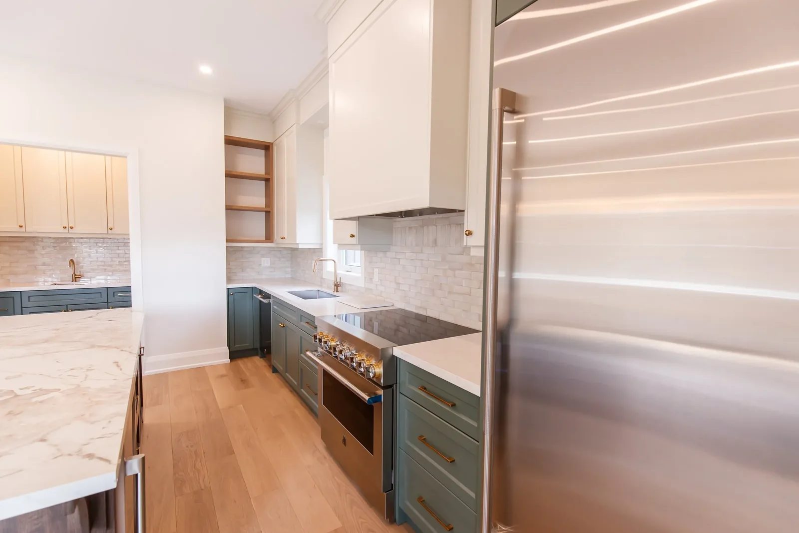 Wide galley view of a finished two-tone kitchen with oak floors, marble island, and pro range along the run.