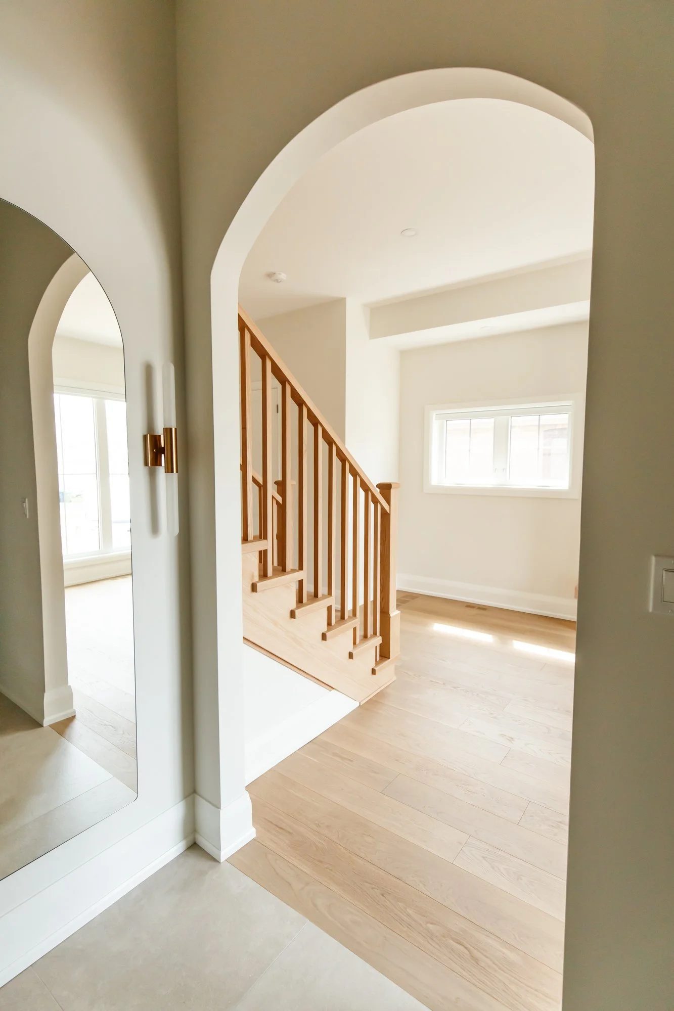 Warm white entry with an arched opening, natural oak stairs, pale floors, and clean Toronto renovation detailing.