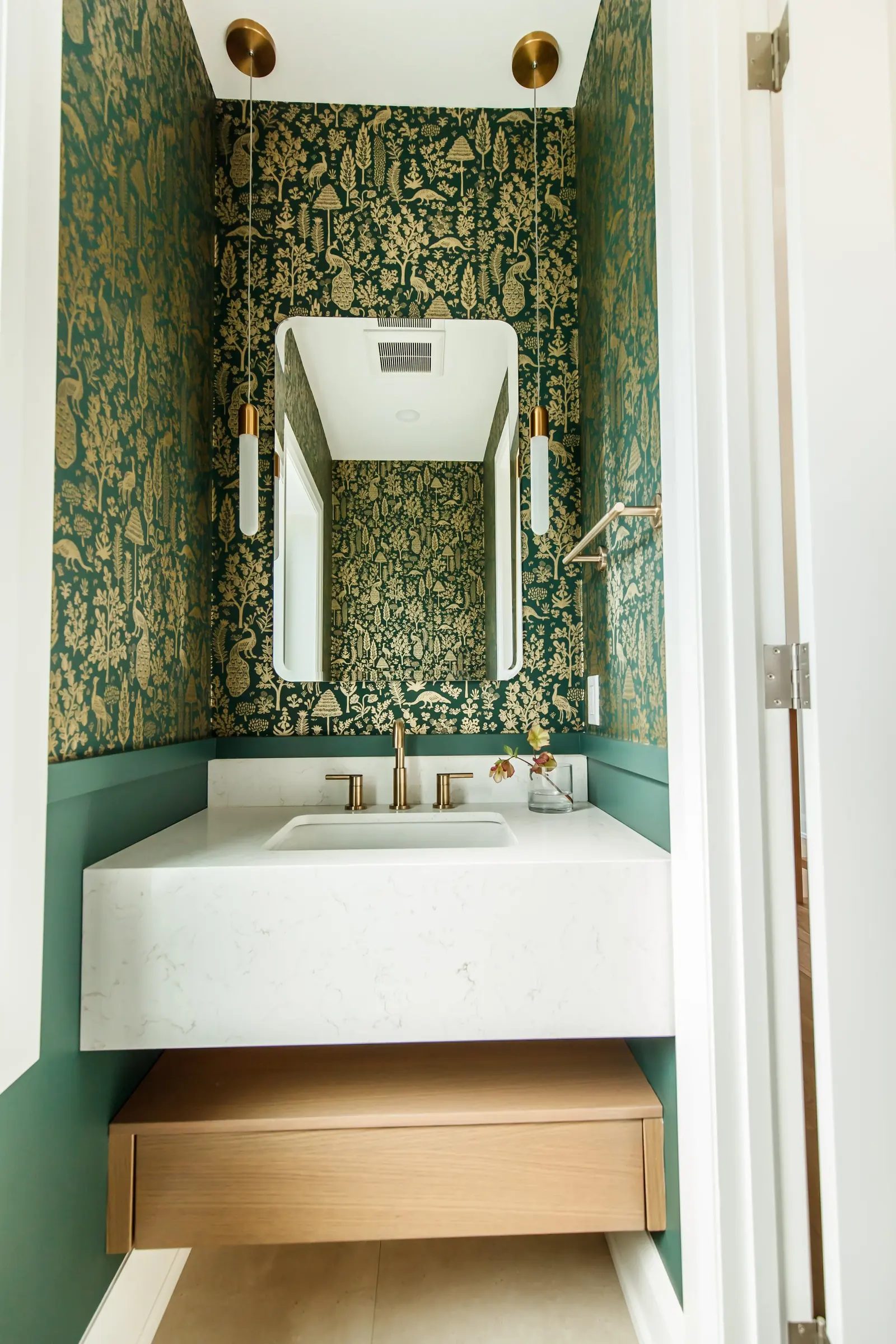 Powder room with a floating oak vanity and arched mirror against green botanical wallpaper.