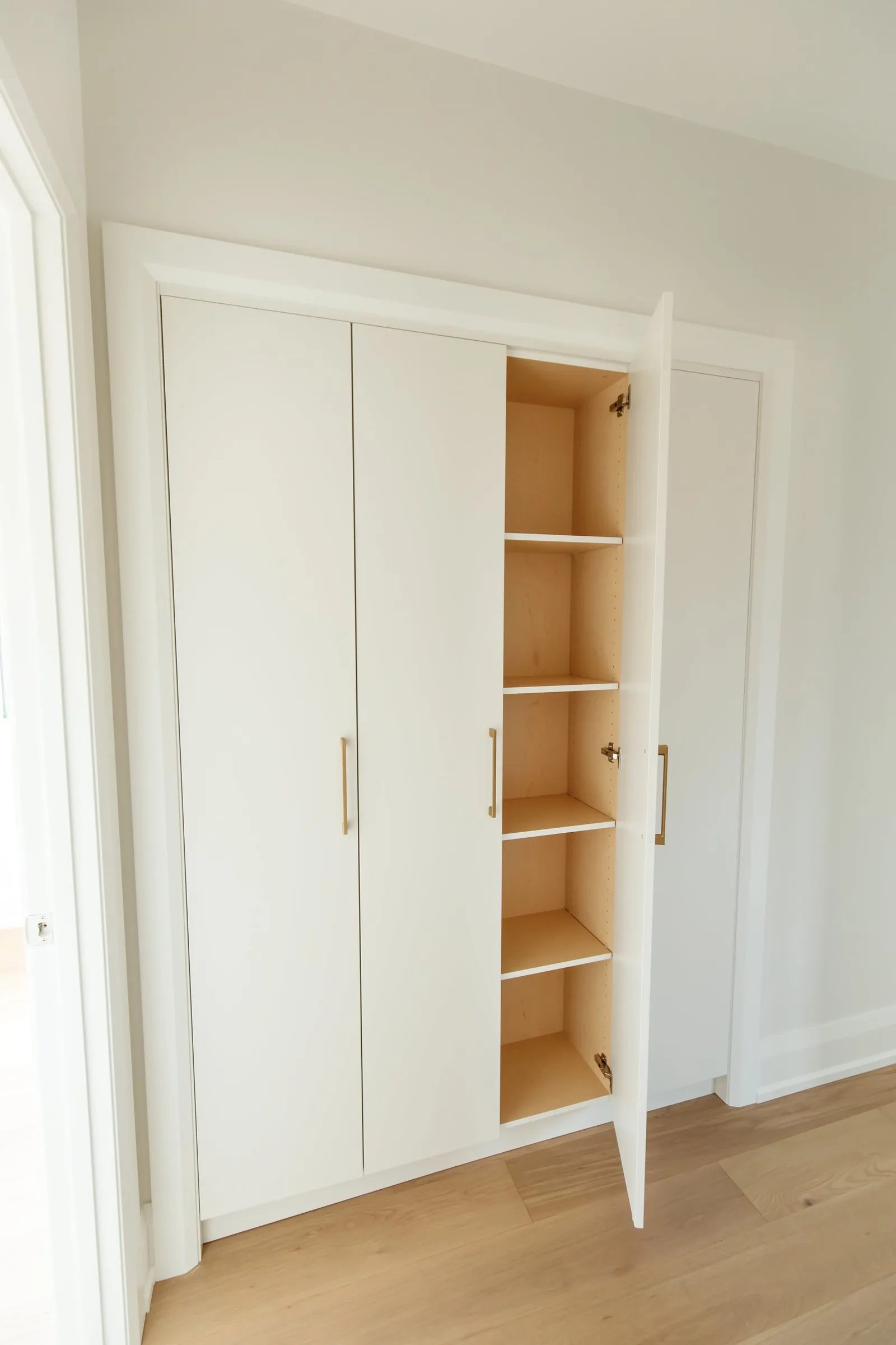 Built-in linen closet with open door revealing birch plywood interior and adjustable shelves.