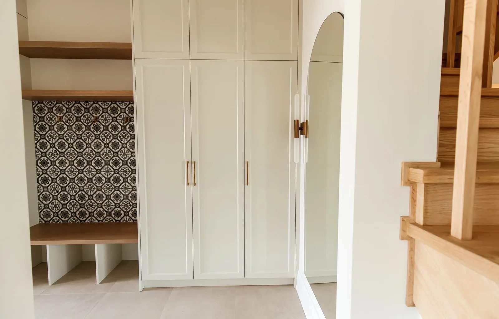 Built-in cream mudroom meets a white oak open-tread stair with an arched mirror accent.